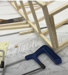 Wooden frame sits on top of plans and a hacksaw