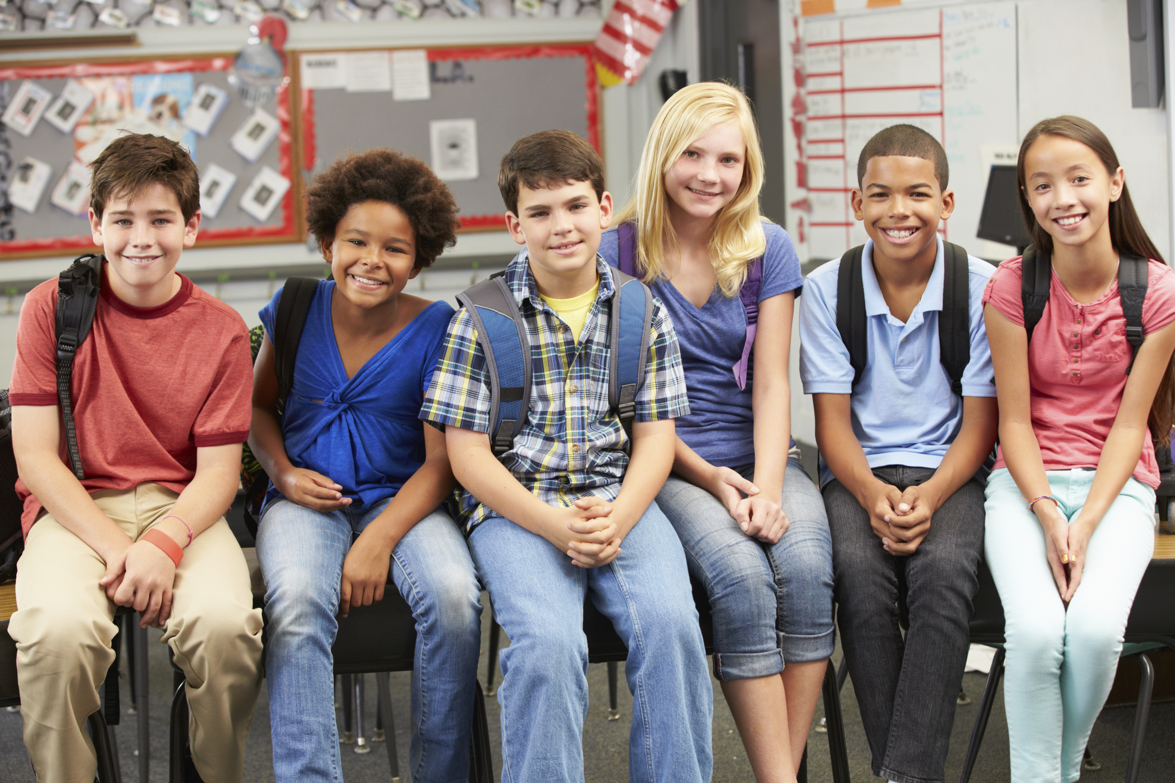 Six students with backpacks sitting on wall