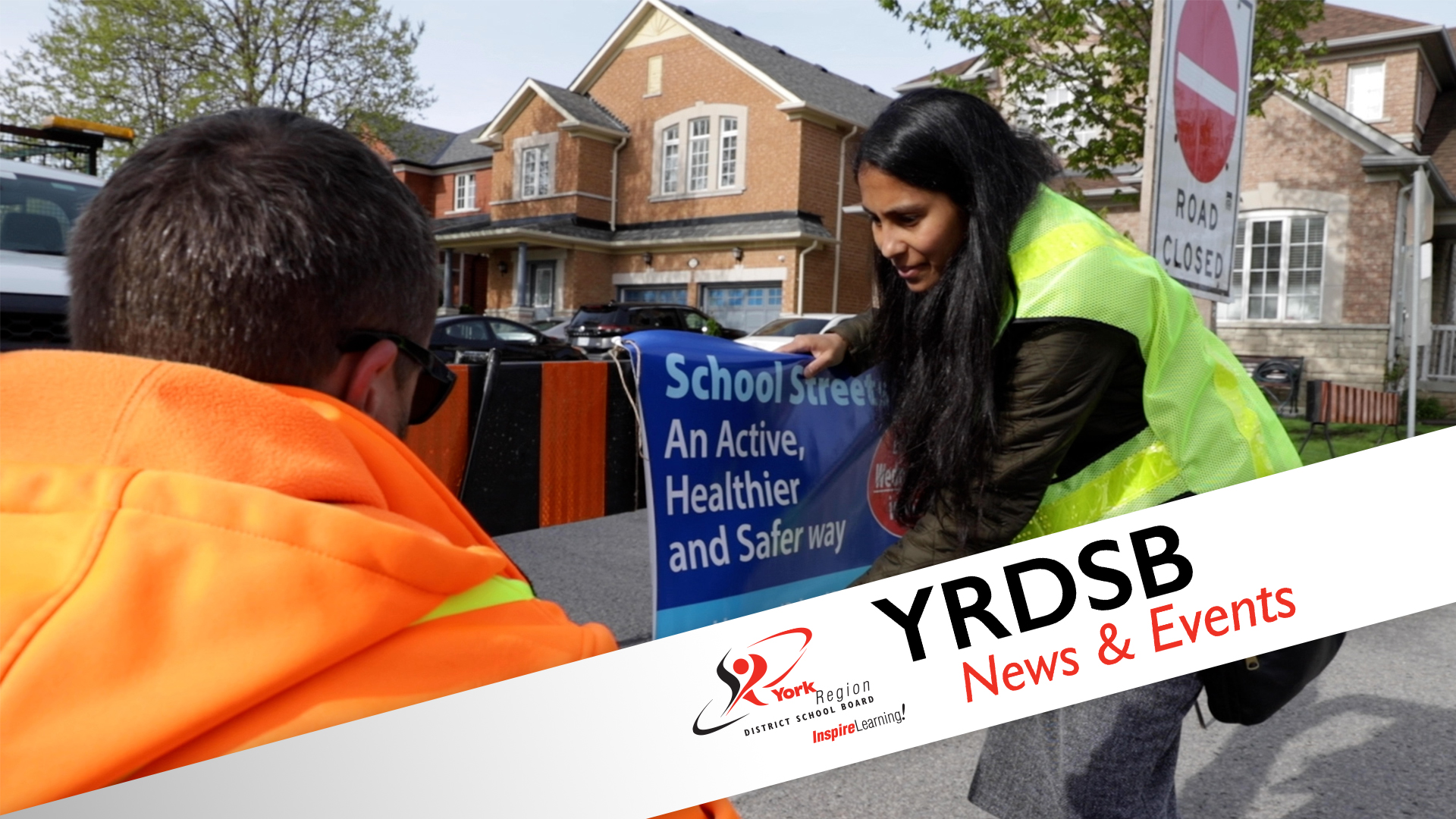 Two people displaying school streets sign with houses behind them