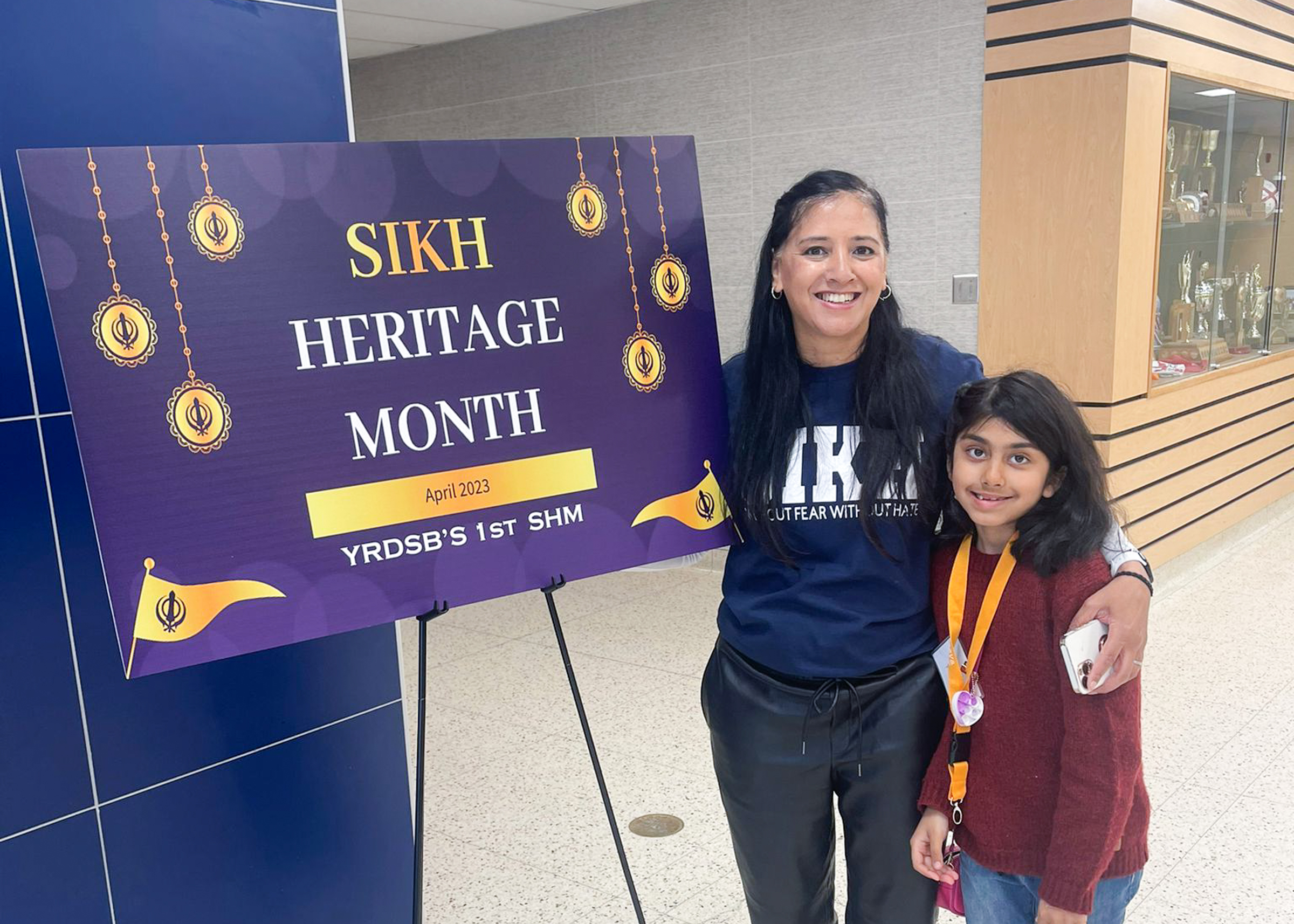 Young student and adult standing beside purple sign reading "Sikh Heritage Month"
