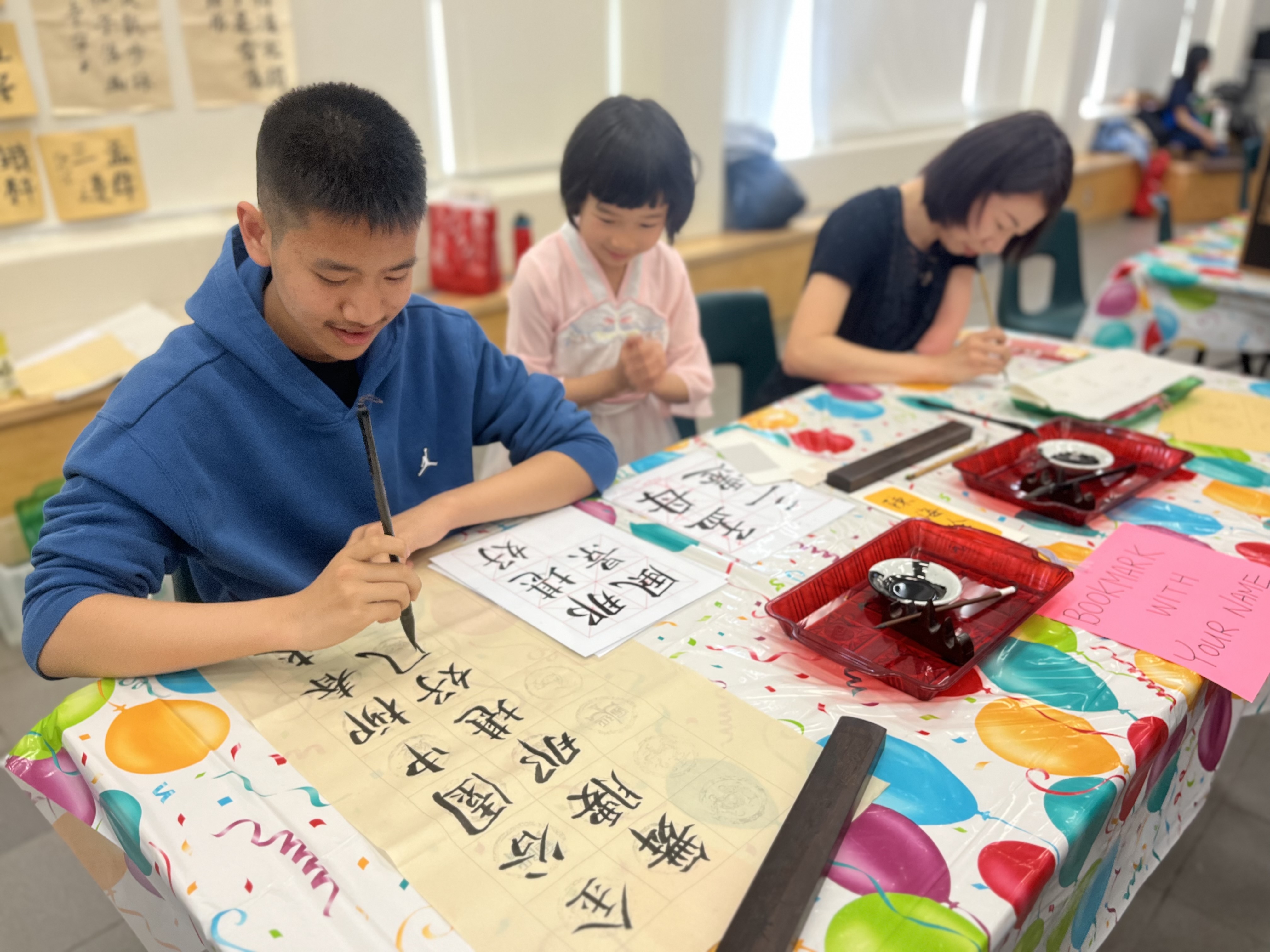 Three students seated at a table writing in calligraphy