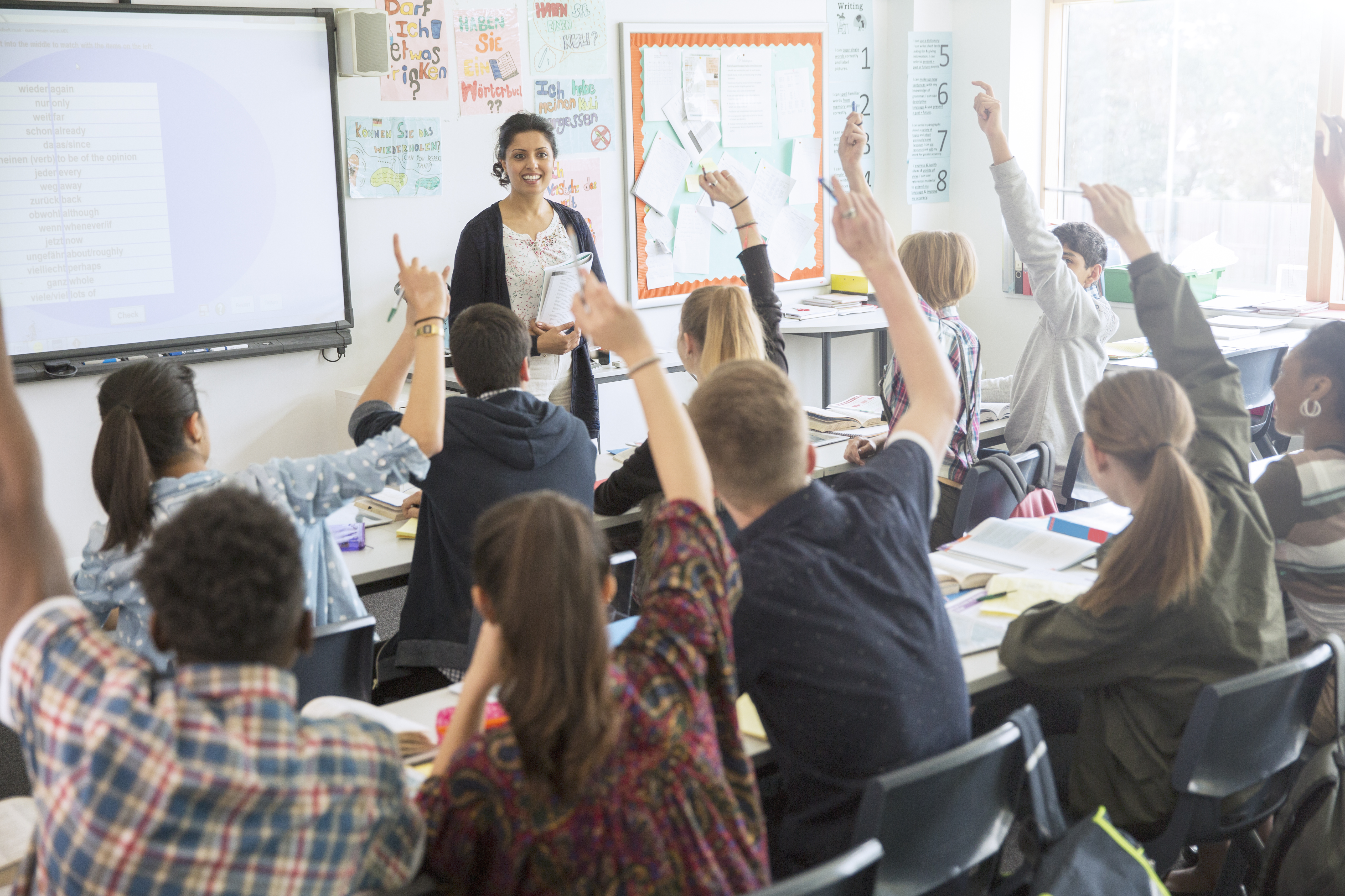 Secondary Seconds in a classroom with hands up