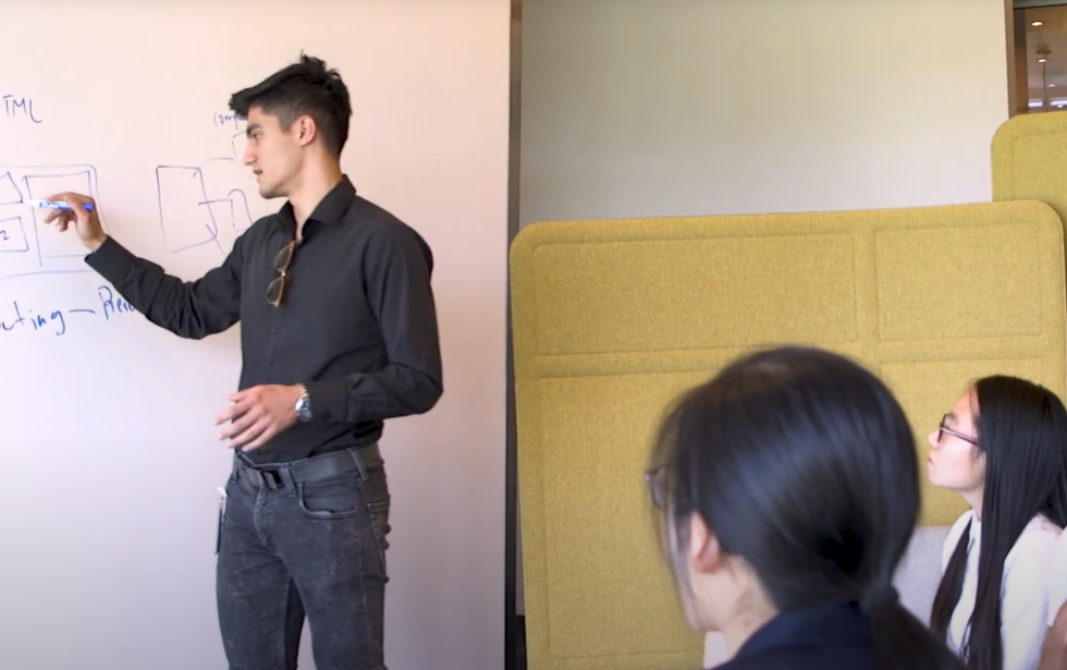 Student writes on a whiteboard while two other students watch