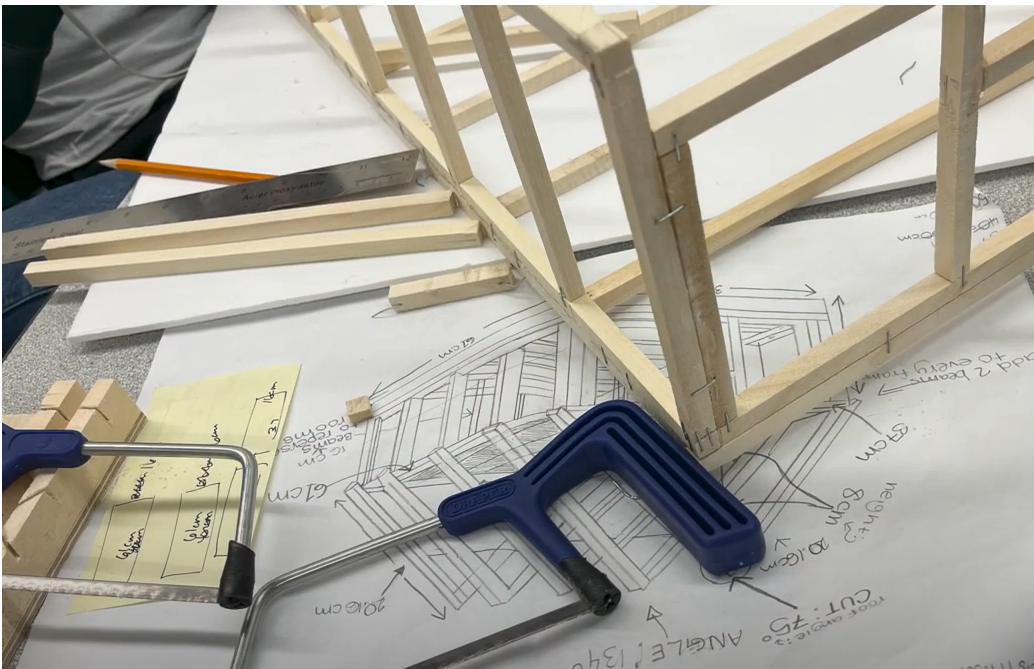 Wooden frame sits on top of plans and a hacksaw
