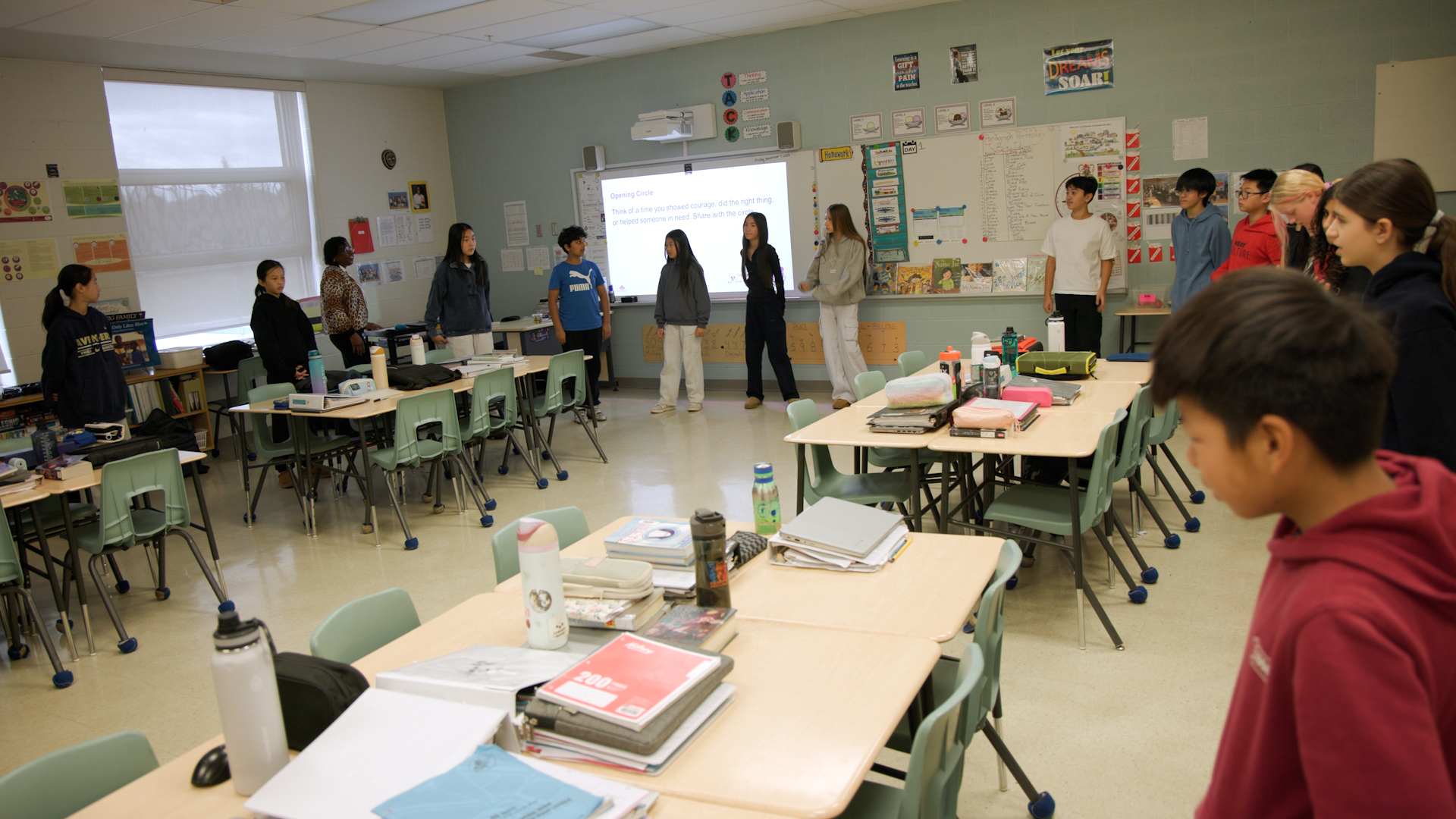 Students stand against the wall around the outside of a classroom