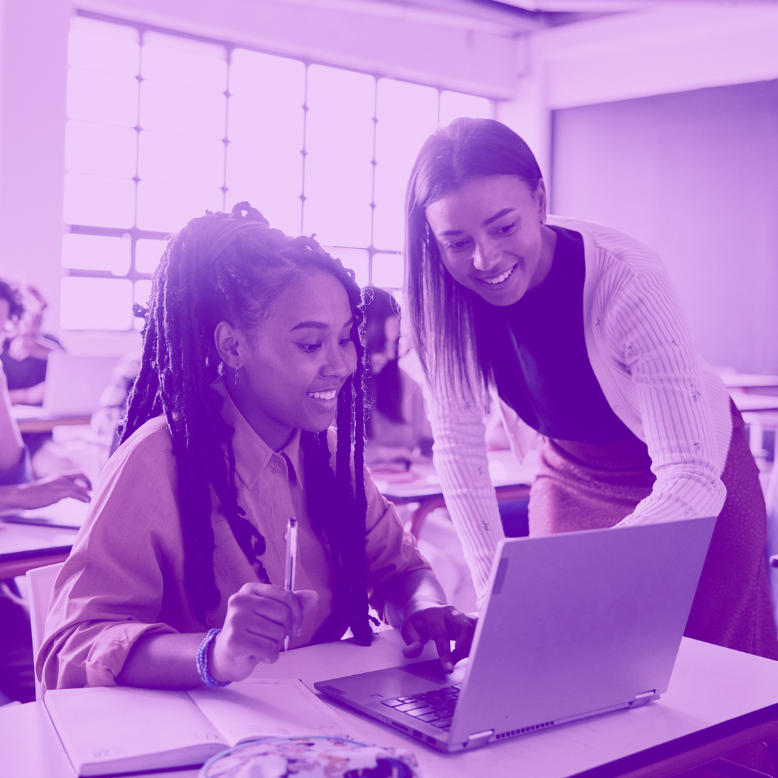 Student and teacher look at computer screen. Image has purple tint to it. 