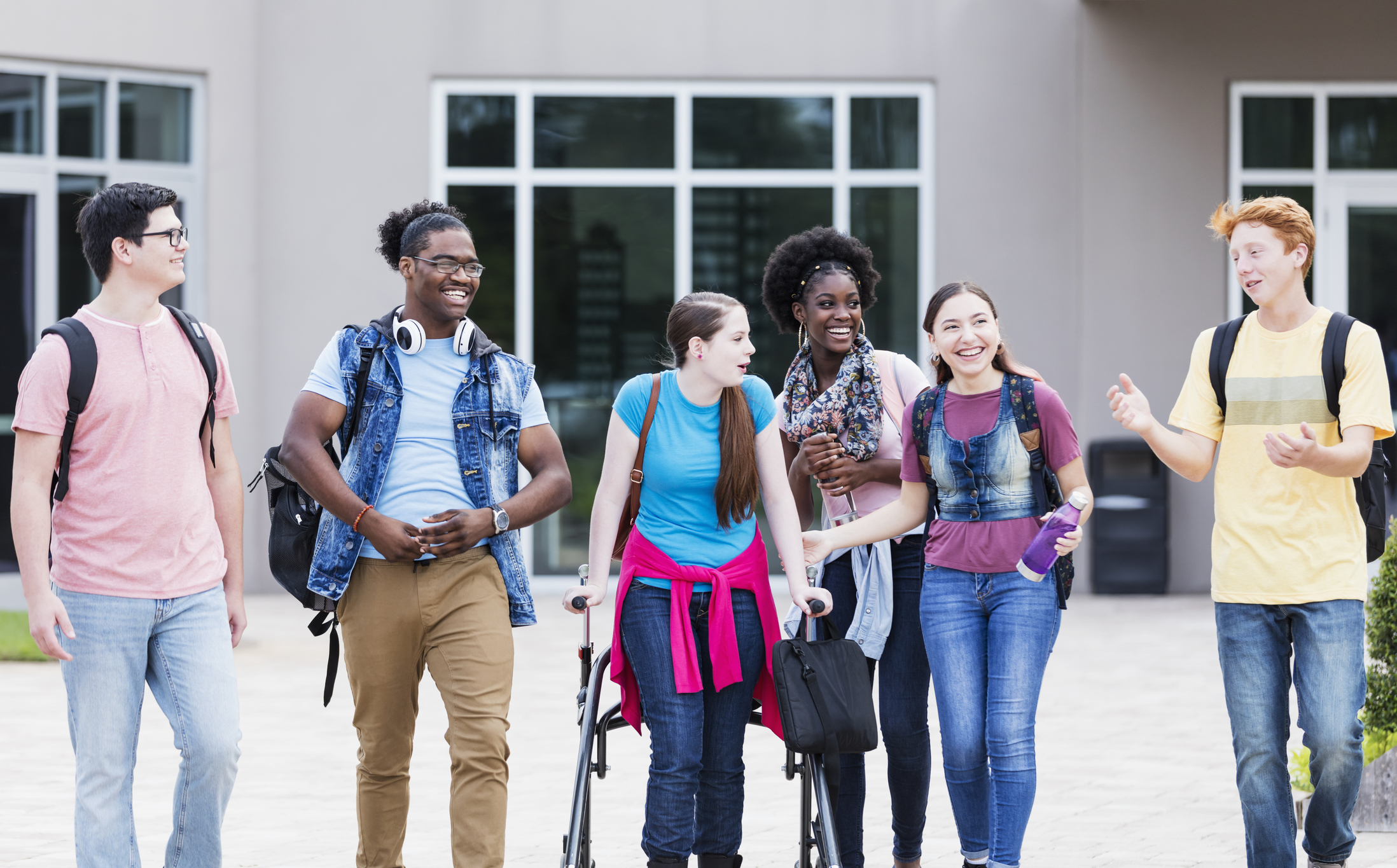 Students including one with a mobility device walking outside of a school building