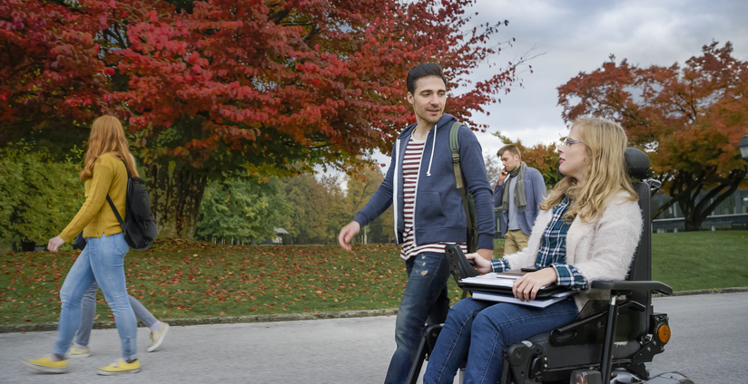 Student walking with student in wheelchair outside