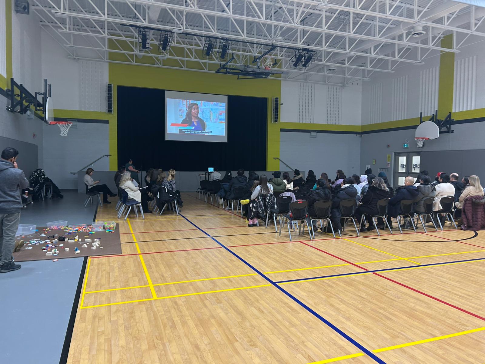 Families seated in a school gym watching a video as part of the presentation.