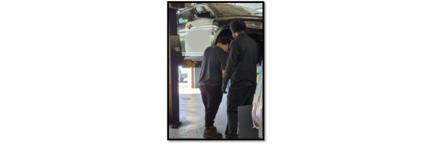Ryan and a Goodyear employee standing next to a car that is raised on a lift at Goodyear.