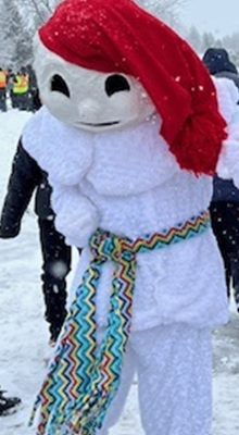 Image of an individual dressed up as a snowman with a red sock hat and a geometric turquoise, yellow, red, navy scarf tied around their waist