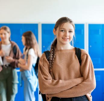 female secondary student standing backpack lockers