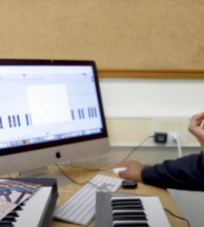 Student wearing headphones sits in front of music keyboard and monitor 