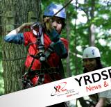 Student strapped onto wires, tree top trekking in the trees. 