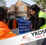 Two people displaying school streets sign with houses behind them