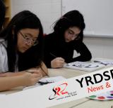 Two students sitting at table painting with paint pallet beside them