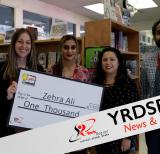 Students and adults holding large check for $1000 in school library