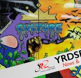 Brightly coloured mural with image of graduation cap, crown, birds, branches and fist holding broken chain