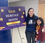 Young student and adult standing beside purple sign reading "Sikh Heritage Month"