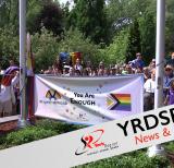 Large group of students and staff stand behind two flag poles. A sign between the flag poles reads you are enough and has the progress pride flag on it.