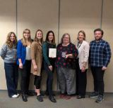 Adults standing in front of wall holding awards
