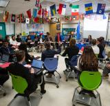 students sit at desks in classroom facing centre of room. Flags from different countries hang across the ceiling.
