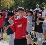 Student wearing red shirt stretches arms. Behind him, other students and educators also stretch. 