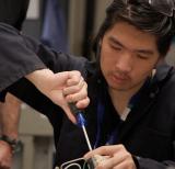 Student wearing coveralls uses tool to fix an item