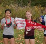 three students stand outside holding medals and a pennant that reads 2025-2026 Senior Girls YREAA Cross Country