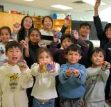 Students stand together in a group in a classroom holding up painted rocks