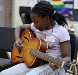 Student holds guitar and plucks at the strings in school music room